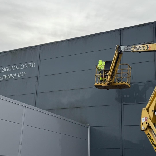 Facaderens på mørk facade ved Løgumkloster Fjernvarme – Dansk Damprens udfører rens med lift.